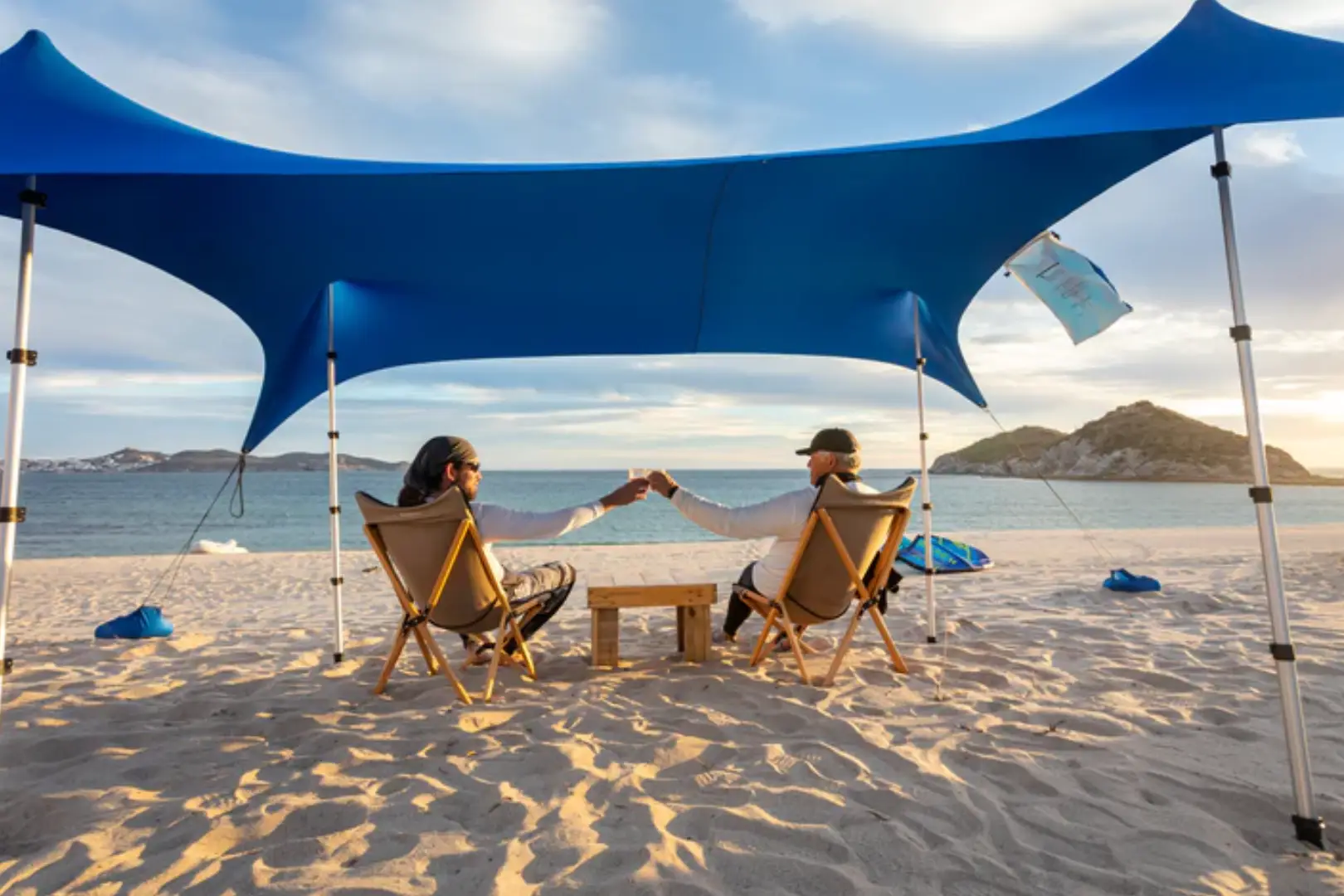 Two people sitting on beach chairs under a blue canopy.