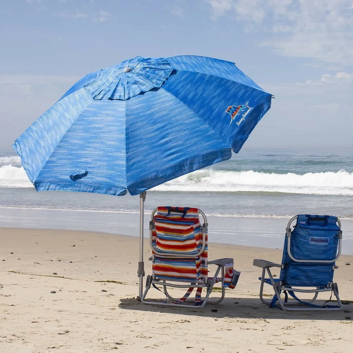 Two lawn chairs under an umbrella on the beach.